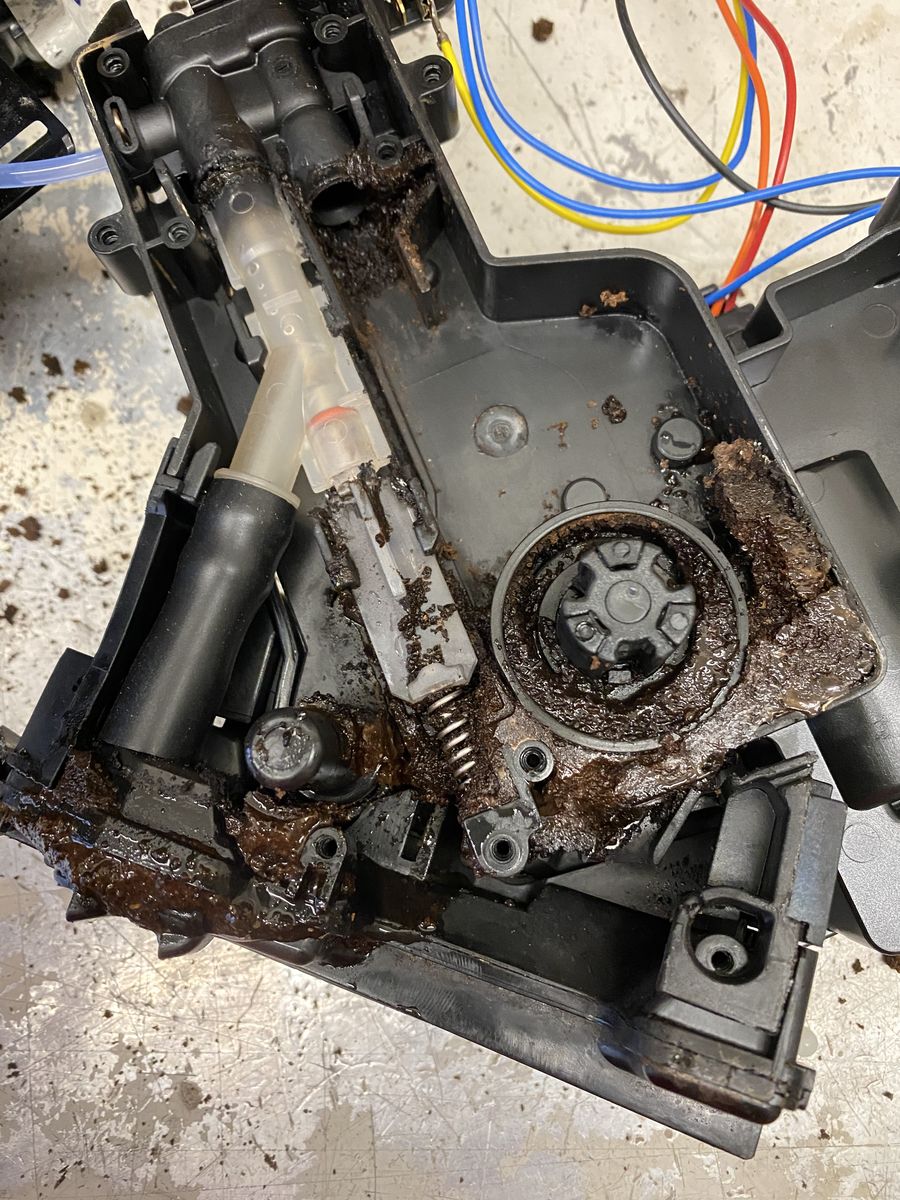 Ausgebaute Baugruppe mit Zahnrad und Kabeln, stark mit Kaffeeresten verschmutzt